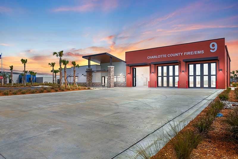 Modern fire station building with "Charlotte County Fire/EMS 9" written on the front, large glass doors, and a wide driveway, photographed at sunset in Southwest Florida.
