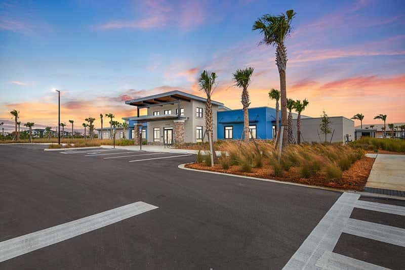 Modern commercial building with large windows, surrounded by palm trees and an empty parking lot under a colorful Southwest Florida sunset, showcasing expert construction management.