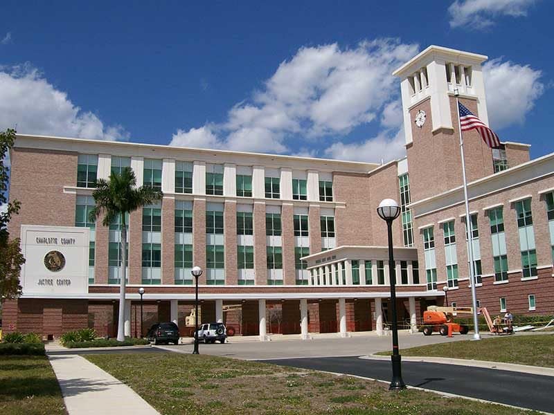 A modern four-story courthouse building with a clock tower, American flag, palm tree, and several parked vehicles in front—an example of Construction Management excellence in Southwest Florida.