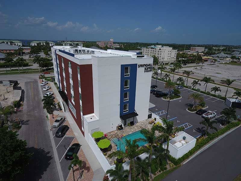 Aerial view of a four-story hotel building with an outdoor pool, surrounded by a parking lot and palm trees in Southwest Florida’s commercial district, showcasing expert construction management.
