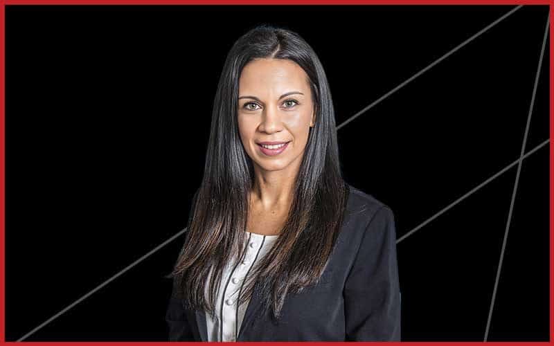 A woman with long straight dark hair, wearing a black blazer over a white top, stands against a black background with diagonal lines and a red border, representing Construction Management in Southwest Florida.