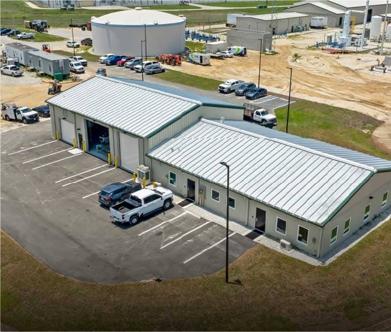 Aerial view of a small industrial facility in Southwest Florida with two metal buildings, several parked vehicles, and surrounding equipment on a paved lot—ideal for construction management operations.