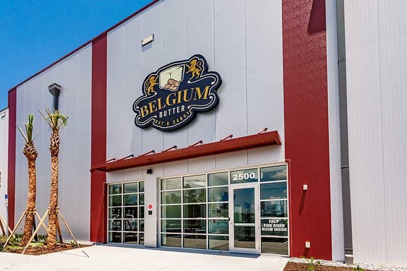 Exterior view of a commercial building in Southwest Florida with a sign reading "Belgium Butter" above the entrance, featuring red accents, palm trees, and large windows—a testament to expert construction management.