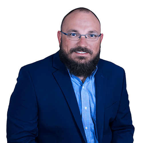 A man with glasses and a beard, dressed in a blue suit jacket and light blue shirt, poses against a plain light background, embodying the professionalism of construction management in Southwest Florida.