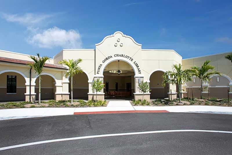 Exterior view of the Punta Gorda Charlotte Library building in Southwest Florida, featuring an arched entryway, palm trees, and a clear sky.