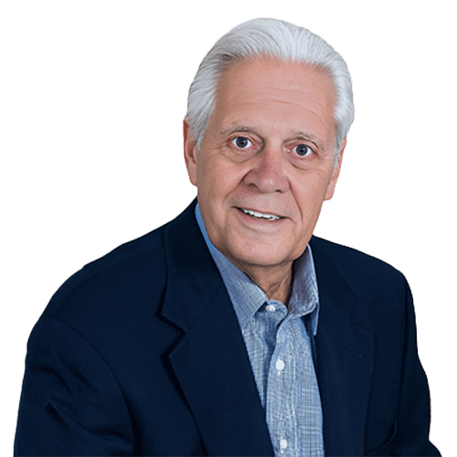Older man with white hair, wearing a navy blazer and light blue shirt, smiles at the camera against a plain light background, reflecting his expertise in Construction Management in Southwest Florida.