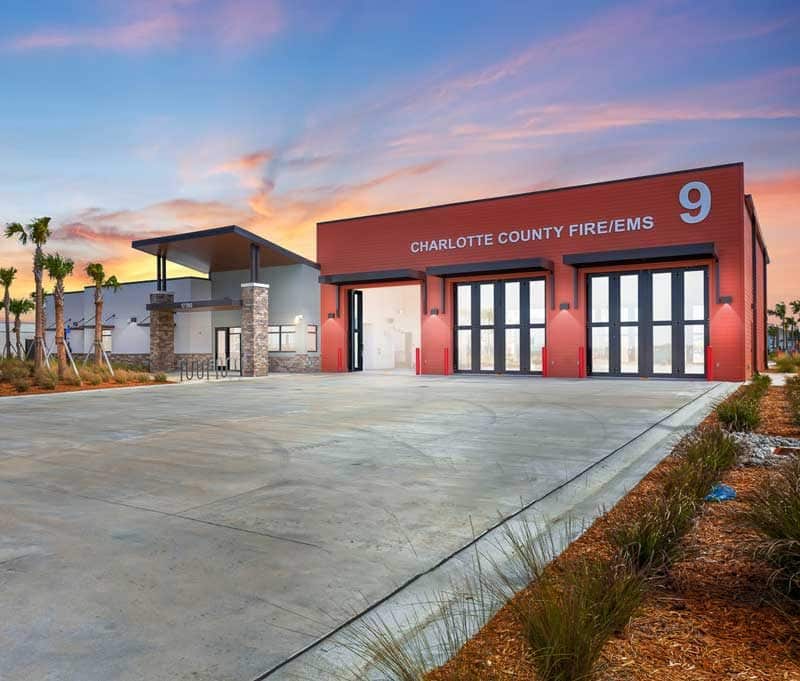 Modern fire station building labeled "Charlotte County Fire/EMS 9" with three large garage doors, surrounded by landscaping, at sunset—a showcase of Construction Management excellence in Southwest Florida.
