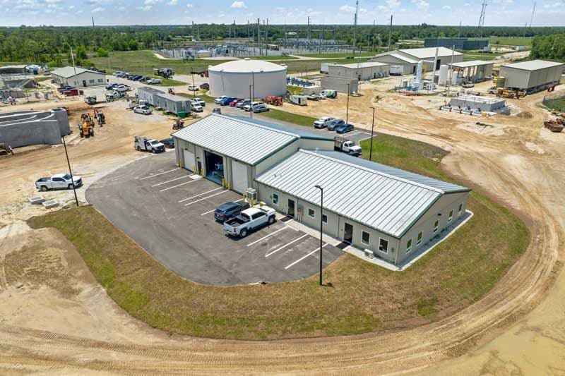 Aerial view of a utility facility in Southwest Florida with several metal buildings, parked vehicles, and equipment, surrounded by dirt roads and grassy areas—a hub for construction management operations.