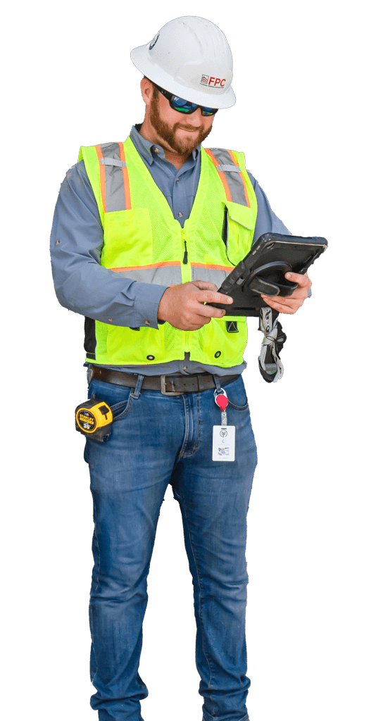 A construction worker wearing a hard hat, safety vest, and sunglasses stands while using a tablet, demonstrating modern Construction Management practices in Southwest Florida.